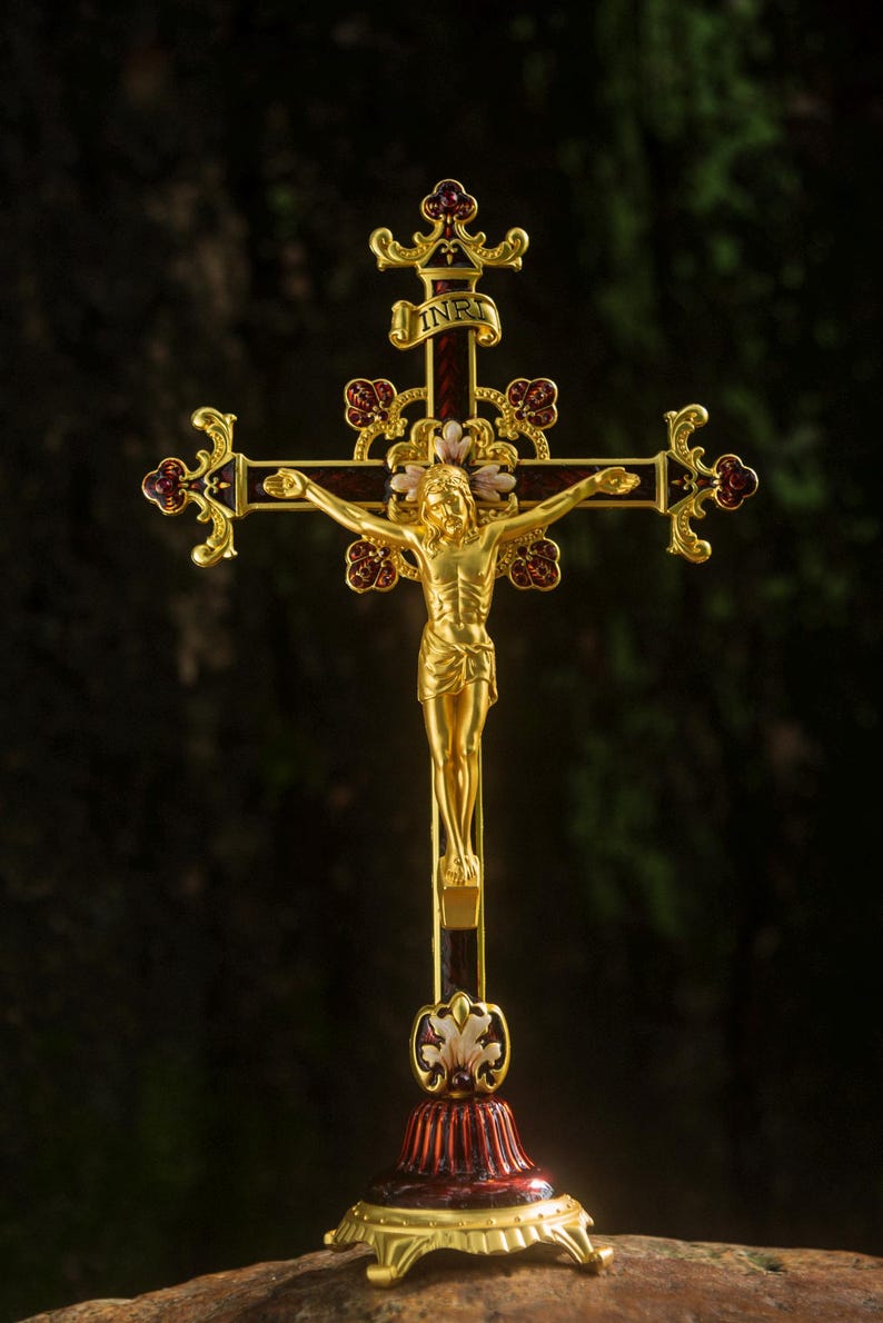 K&ouml;nnte beinhalten: Ein goldfarbenes Kruzifix mit einer detaillierten Figur Jesu Christi. Das Kreuz weist aufwendige Details mit roten und goldenen Akzenten auf. Der Sockel hat eine passende rot-goldene Farbe, und das Kreuz tr&auml;gt oben die Buchstaben INRI.