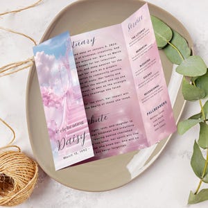 May include: A pink and white tri-fold funeral program with a photo of a stairway to heaven and the words "Celebrating Daisy" on the front. The program includes the dates "January 8, 2024" and "March 15, 1992" and the words "Service", "The Liturgy", "Memorial", "Blessing", "Eulogy", "Recessional", and "Pallbearers".