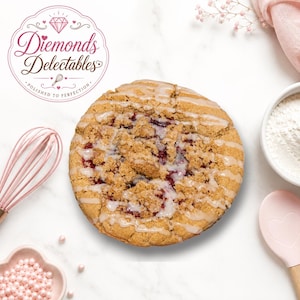 May include: A round berry crumble cake topped with a white sugar glaze, positioned near a pink whisk, a small bowl of pink sprinkles, a bowl of white flour, and a pink heart-shaped spatula. The logo reads Diemonds Delectables.