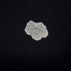 Puede incluir: Primer plano de una tela negra con un diseño de hoja blanca. La hoja tiene detalles de venas negras. La tela tiene una textura sutil y el diseño está centrado, creando una estética simple pero elegante.