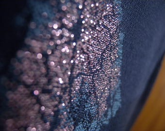 Könnte beinhalten: Nahaufnahme eines dunkelblauen Stoffes mit einem schimmernden, glitzernden Muster in Rosa- und Silbertönen. Der Stoff hat ein strukturiertes Aussehen, wobei der Glitzer einen funkelnden Effekt erzeugt. Das Design ist abstrakt und dekorativ.