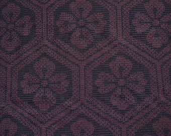 Könnte beinhalten: Nahaufnahme eines dunkelroten Stoffes mit einem sich wiederholenden Muster aus kleinen, filigranen Designs. Der Stoff hat eine subtile Textur und eine leicht schimmernde Optik.