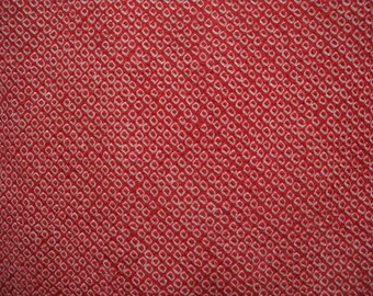 Puede incluir: Primer plano de una tela roja con un patrón repetitivo de pequeños diseños cuadrados blancos. El patrón está espaciado uniformemente, creando una apariencia texturizada. El color de la tela es un rojo vibrante y sólido.