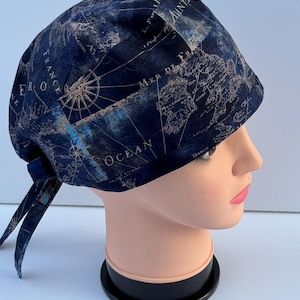 May include: A navy blue surgical scrub cap featuring a vintage map design with compass rose details. The cap is made of fabric and has ties at the back for an adjustable fit. The map includes the words "France" and "Ocean".