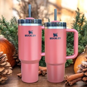 May include: Two pink Stanley travel mugs with black handles and lids. Both mugs have a black logo with a bear and the word "STANLEY".
