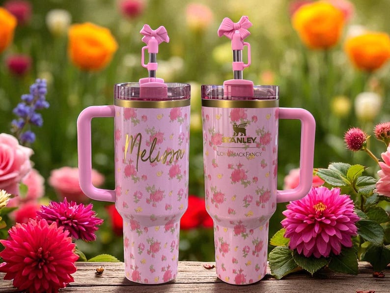 May include: Two pink Stanley tumblers with floral patterns and pink handles. One tumbler has the name "Melissa" in gold script, and the other has the Stanley logo. Both have pink bow-shaped toppers.