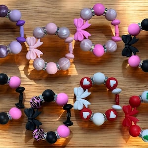 Puede incluir: Surtido de diez pulseras de dentición de silicona de colores con varios diseños, incluyendo lazos, corazones y árboles de Navidad. Las pulseras están hechas de silicona suave y masticable y son perfectas para bebés y niños pequeños.