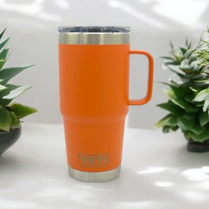 May include: Orange stainless steel travel mug with a handle. The mug has a Yeti logo on the side.