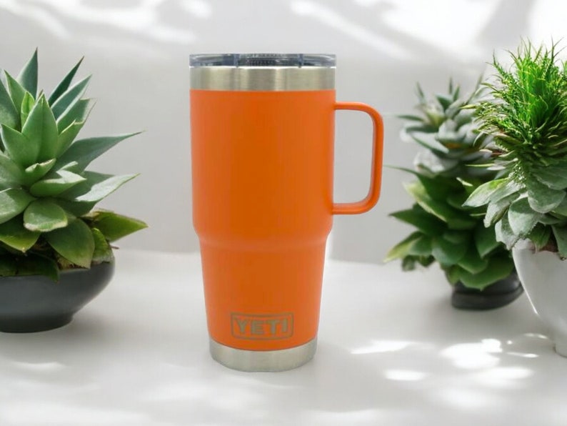 May include: Orange stainless steel travel mug with a handle. The mug has a Yeti logo on the side.