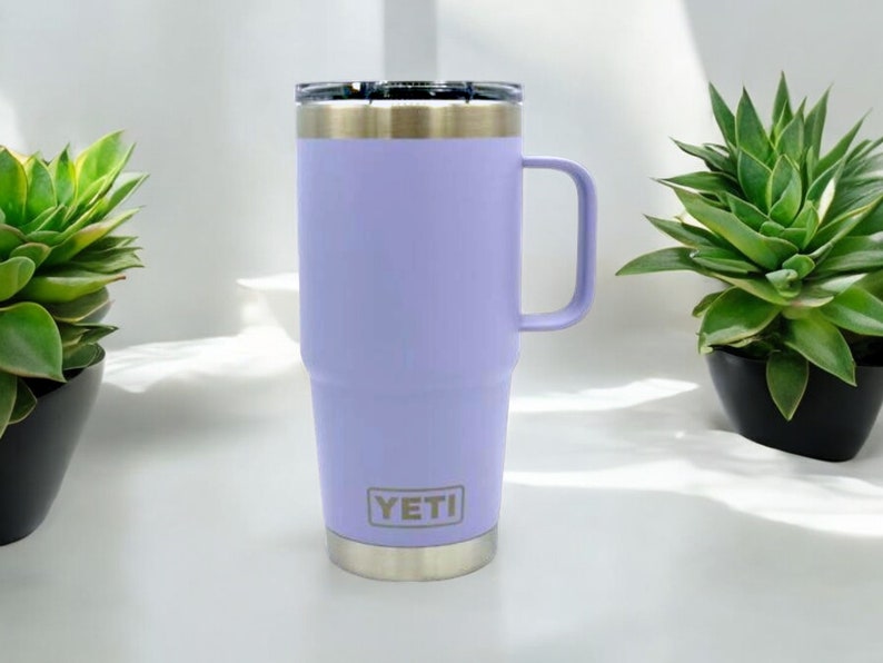 May include: A purple YETI Rambler travel mug with a stainless steel lid and handle. The mug has a YETI logo on the side.