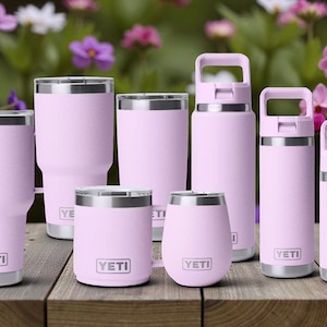 May include: A selection of pink insulated drinkware, including tumblers, bottles, and wine glasses, with silver rims and the "YETI" logo. The drinkware is displayed on a wooden surface with a blurred floral background.