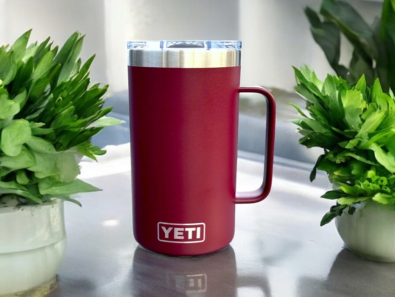 K&ouml;nnte beinhalten: Eine burgunderrote YETI Rambler 14 oz Tasse mit einem Edelstahldeckel und einem Griff.