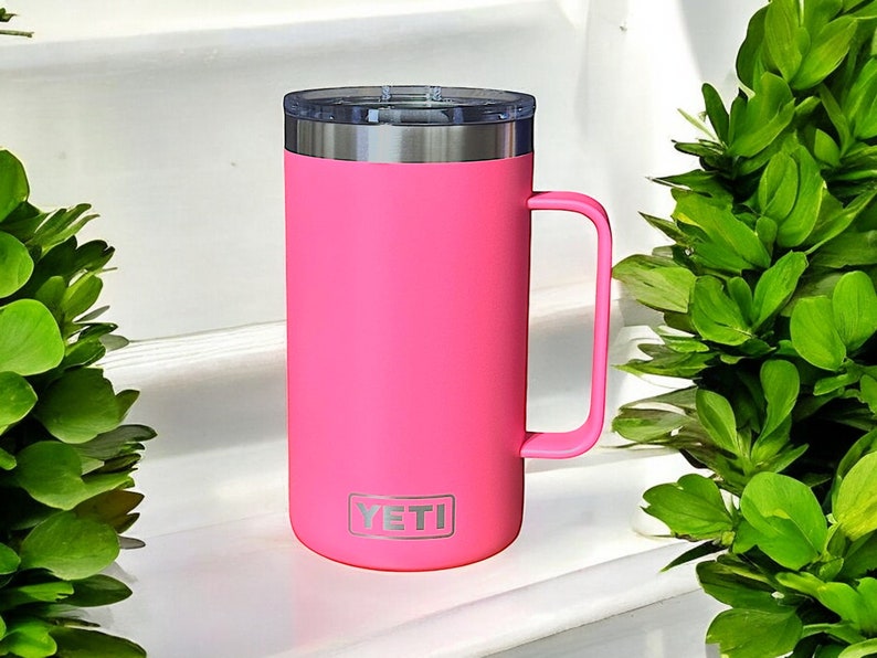 K&ouml;nnte beinhalten: Eine rosa YETI Rambler 14 oz Tasse mit einem Edelstahldeckel und einem Griff.