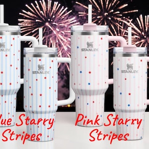May include: Four Stanley tumblers with lids and handles. Two are white with blue stripes and red stars, the other two are white with pink stripes and red and blue stars. The text "Blue Starry Stripes" and "Pink Starry Stripes" is visible.