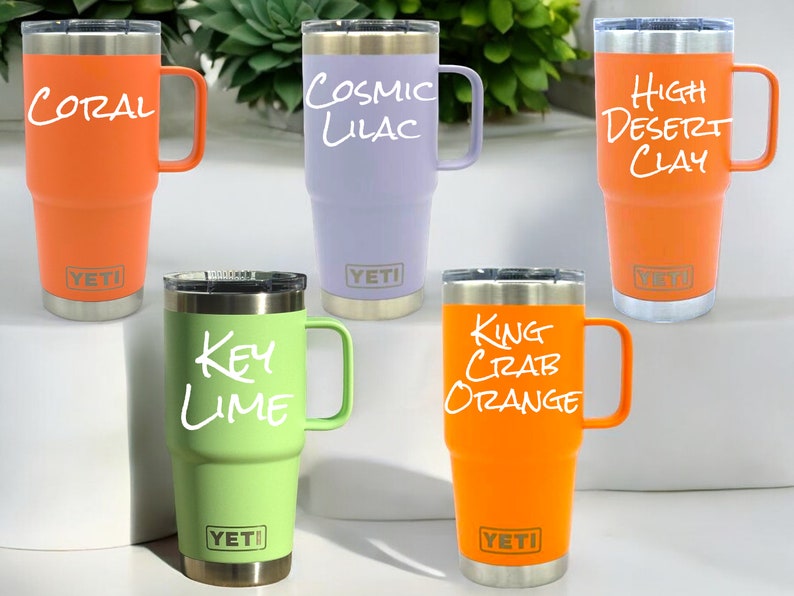 May include: Five YETI Rambler Tumblers with different colored lids and handwritten names on the side: Coral, Cosmic Lilac, High Desert Clay, Key Lime, and King Crab Orange.