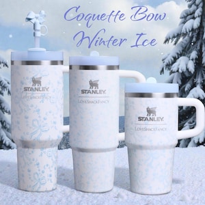 May include: Three Stanley insulated travel mugs and a mug with a light blue floral pattern and lids. The mugs have the text "Stanley" and "LoveshackFancy". The image has the text "Coquette Bow Winter Ice".