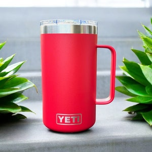 K&ouml;nnte beinhalten: Eine rote YETI Rambler 14 oz Tasse mit einem Edelstahldeckel und -griff. Die Tasse steht auf einer grauen Oberfl&auml;che.