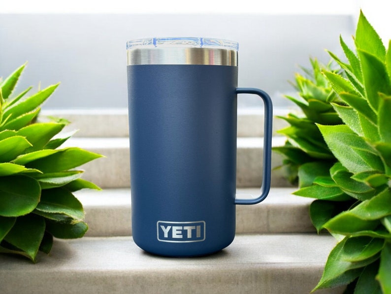 K&ouml;nnte beinhalten: Eine blaue YETI Rambler 14 oz Tasse mit einem Edelstahldeckel und -griff. Die Tasse steht auf einer Betontreppe.