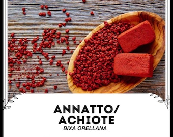 Peut inclure: Un bol en bois rempli de graines d'annatto rouges, également appelées achiote, avec deux blocs de pâte d'annatto. Le texte "Annatto/Achiote Bixa Orellana" est écrit sous le bol.