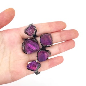 May include: Five rings with purple amethyst stones set in silver settings. The rings are displayed on a hand.