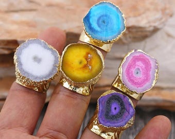 Könnte beinhalten: Fünf goldene Ringe mit verschiedenen farbigen Achat-Steinen. Die Ringe zeigen eine Vielzahl von Farben, darunter Blau, Gelb, Weiß, Rosa und Lila.