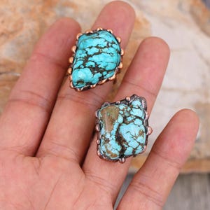 May include: Two turquoise rings with copper settings. The rings feature a unique, irregular shape and a mottled turquoise stone.