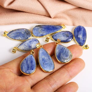 May include: A collection of blue kyanite gemstone pendants with gold-toned accents. The pendants are in various shapes, including teardrop and oval.