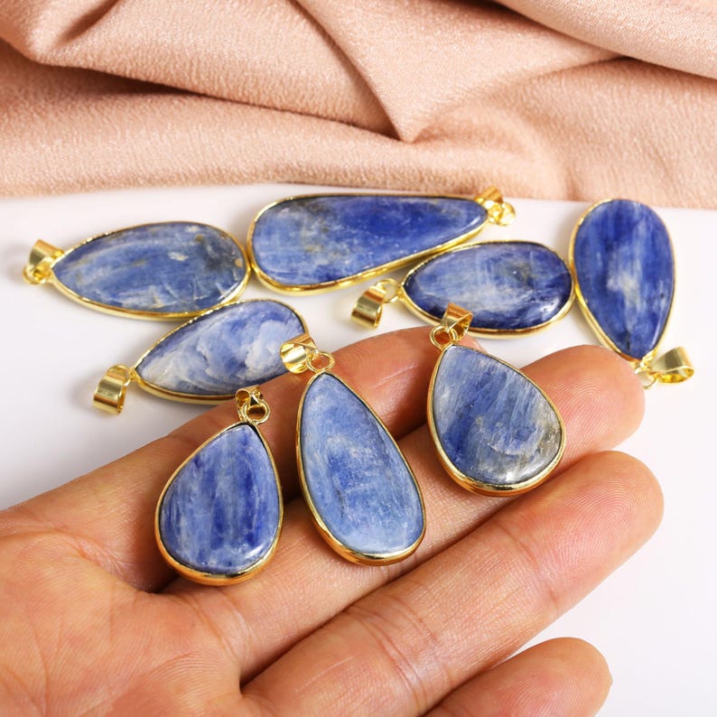 May include: A collection of blue kyanite gemstone pendants with gold-toned accents. The pendants are in various shapes, including teardrop and oval.