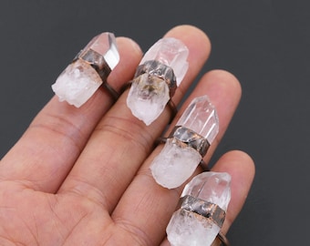 May include: Four rings with clear quartz crystals set in copper bands. The rings are worn on a hand, with each finger displaying a different ring.