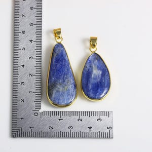 May include: Two teardrop-shaped pendants with gold-toned metal settings and blue gemstone inlays. The pendants are shown next to a ruler, with the larger pendant measuring approximately 5 cm in length and the smaller pendant measuring approximately 4 cm in length.