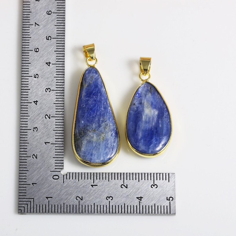 May include: Two teardrop-shaped pendants with gold-toned metal settings and blue gemstone inlays. The pendants are shown next to a ruler, with the larger pendant measuring approximately 5 cm in length and the smaller pendant measuring approximately 4 cm in length.