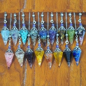 May include: A collection of 18 crystal point pendulums with silver chains and amethyst beads. Each pendulum is filled with different colored crystals and stones.