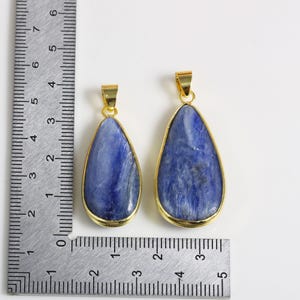 May include: Two blue gemstone pendants with gold-toned settings. The pendants are in the shape of a teardrop and are approximately 5 cm and 7.5 cm in length.