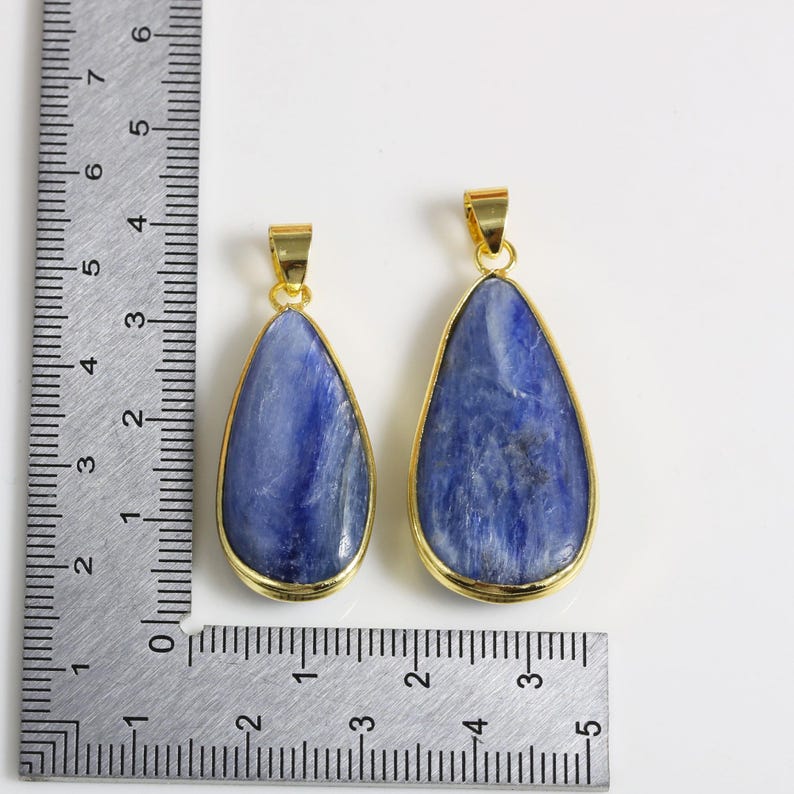 May include: Two blue gemstone pendants with gold-toned settings. The pendants are in the shape of a teardrop and are approximately 5 cm and 7.5 cm in length.