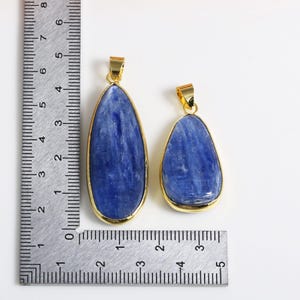 May include: Two blue kyanite gemstone pendants with gold-toned settings. The larger pendant measures approximately 5 cm in length and the smaller pendant measures approximately 3.8 cm in length.