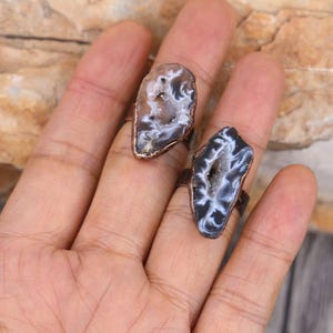 May include: Two rings made with copper wire and natural agate slices. The agate slices are a light brown color with white and black patterns inside. The rings are worn on a person's hand.