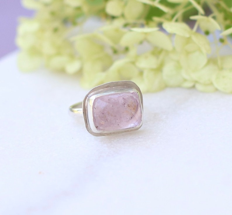 May include: A silver ring with a light pink rectangular gemstone set in a bezel setting.
