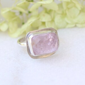 May include: A silver ring with a light pink, rectangular gemstone set in a bezel setting.