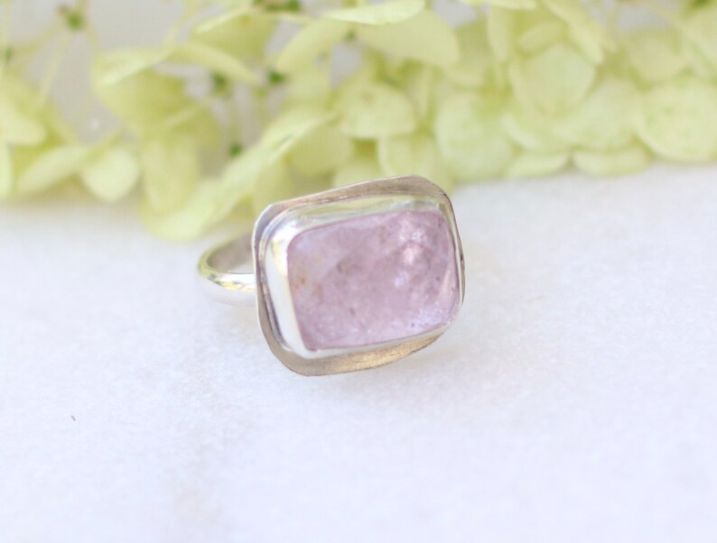 May include: A silver ring with a light pink, rectangular gemstone set in a bezel setting.