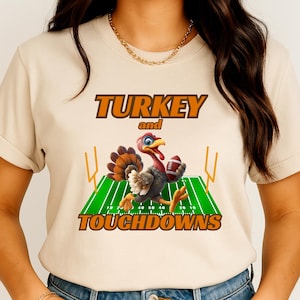 May include: Beige t-shirt with a cartoon turkey holding a football on a green field with yard lines. The text "TURKEY and TOUCHDOWNS" is printed above and below the turkey graphic in orange.