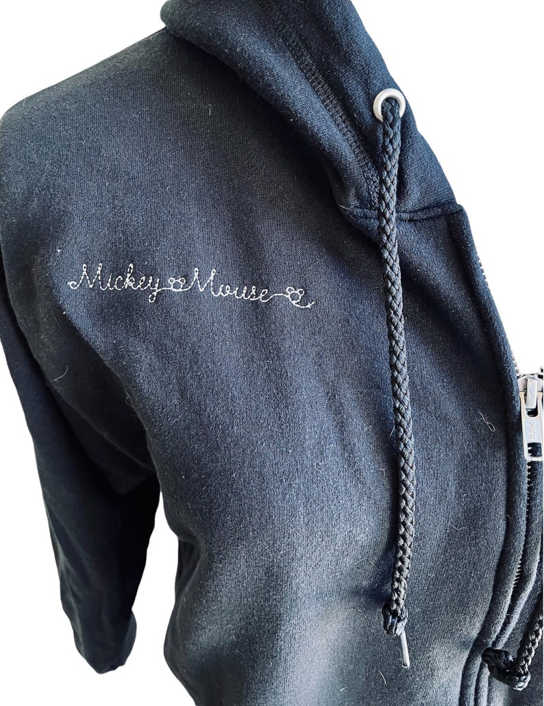 May include: Black zip-up hoodie with a white embroidered design that says "Mickey Mouse" with a heart symbol between the words.
