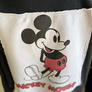 May include: Black and white image of Mickey Mouse on a white background with the text "Mickey Mouse" below him. The image is on a black fabric.