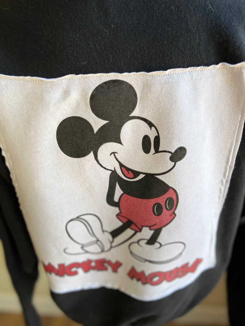 May include: Black and white image of Mickey Mouse on a white background with the text "Mickey Mouse" below him. The image is on a black fabric.