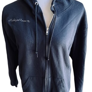 May include: Black zip-up hoodie with a white embroidered design that says "Mickey Mouse" on the front.