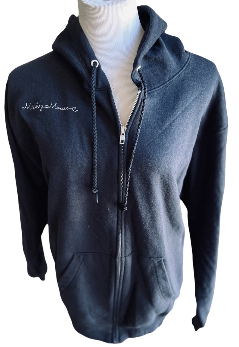 May include: Black zip-up hoodie with a white embroidered design that says "Mickey Mouse" on the front.