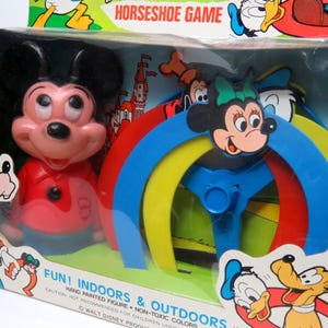May include: A vintage Mickey Mouse horseshoe game with a red, yellow, blue and green plastic ring toss. The game features a hand-painted Mickey Mouse figure and the text "FUN! INDOORS & OUTDOORS HAND PAINTED FIGURE - NON-TOXIC COLORS WALT DISNEY PRODUCTIONS."