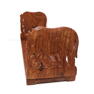 May include: A wooden bookend featuring two intricately carved elephants. The bookend is made of dark brown wood and has a natural finish. The elephants are facing each other and have detailed carvings on their bodies.