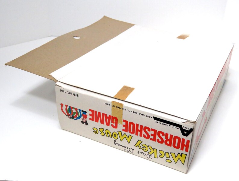 May include: A cardboard box for a Mickey Mouse Horseshoe Game. The box is red, white, and blue with a picture of Mickey Mouse and his friends. The text on the box reads "Mickey Mouse Horseshoe Game" and "Item No. 1106".