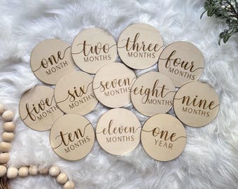 Könnte beinhalten: Ein Satz von 12 Holz-Baby-Meilenstein-Scheiben mit goldener Beschriftung. Die Scheiben zeigen die Zahlen eins bis zwölf mit den Worten "Monat" oder "Monate" und "ein Jahr".
