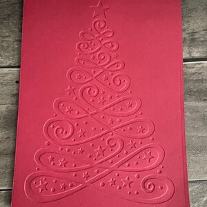 May include: A red card with a white embossed design of a Christmas tree with swirls and stars.